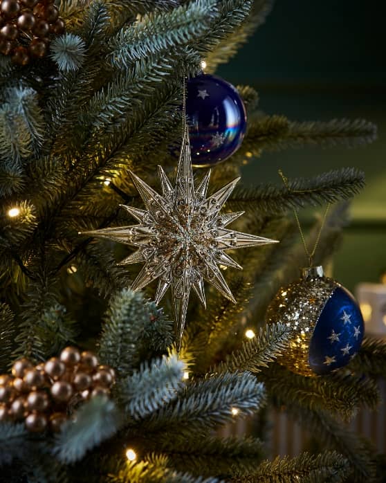 Close-up of Christmas tree with silver star ornament, gold bauble, and warm string lights.