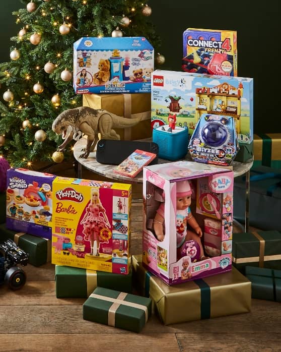 Assorted children’s toys and games stacked near a decorated Christmas tree with wrapped presents.