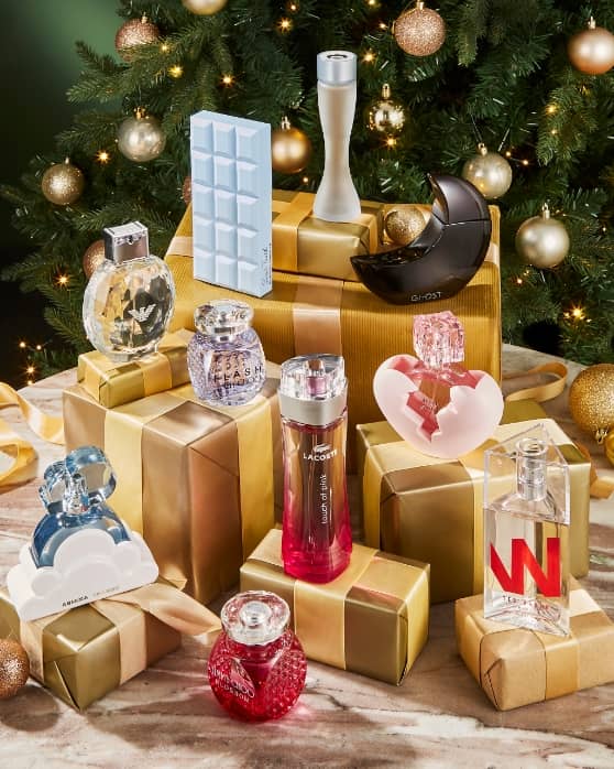Assorted fragrance bottles arranged on gold-wrapped gifts in front of a decorated Christmas tree.