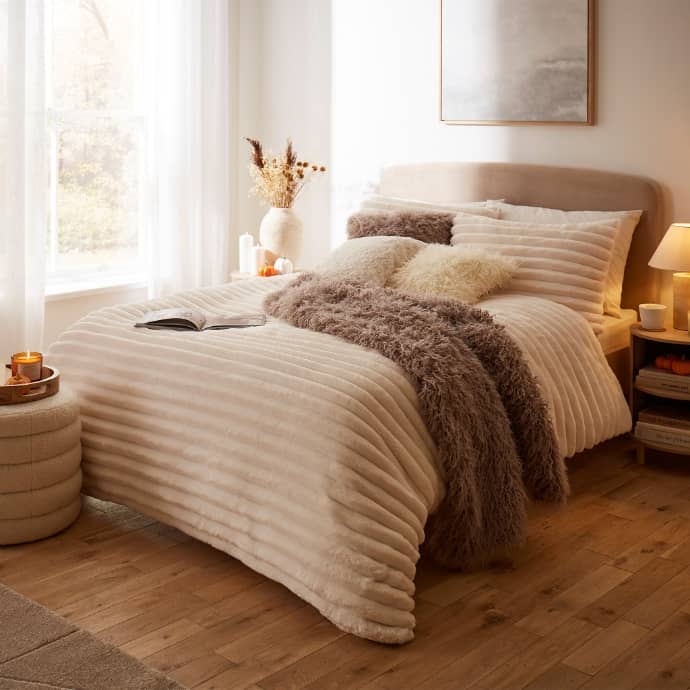 Cosy bedroom with a striped duvet, fluffy throws, cushions, and warm lighting.