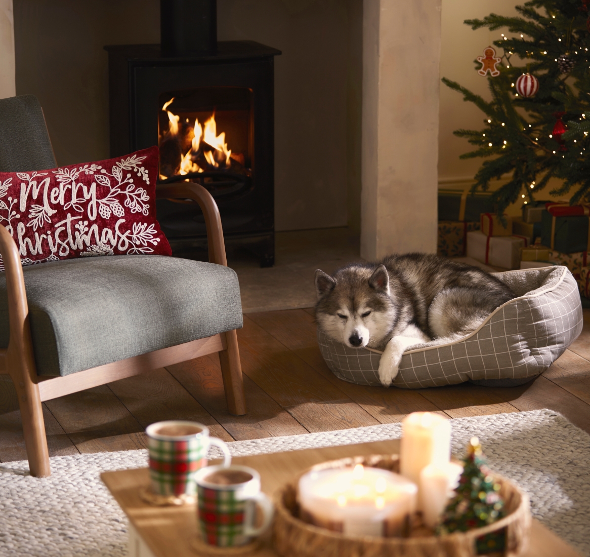 A grey armchair in front of the fire, with a red Christmas cushion.