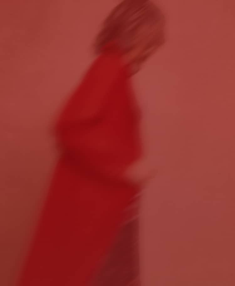 Blurred image of a model in a long red coat against a red-coloured background.