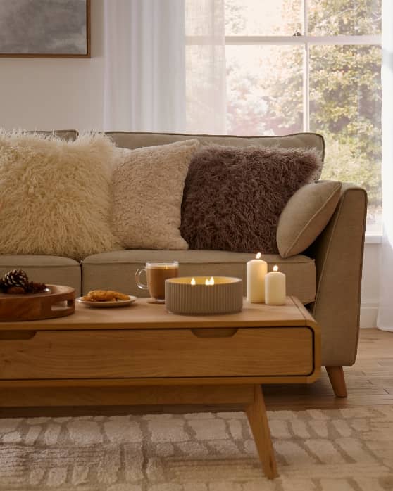 A living room with a sofa and a wooden coffee table with a plate of pastries, a mug, and several lit candles.