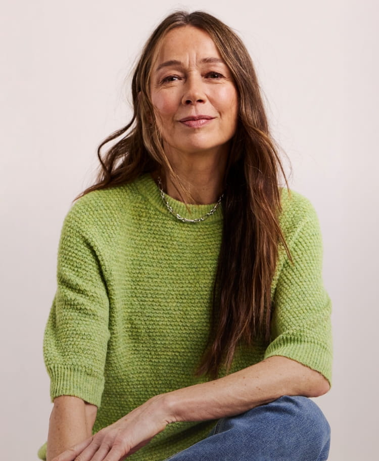 A model sat wearing a green Julipa short sleeve jumper and blue jeans
