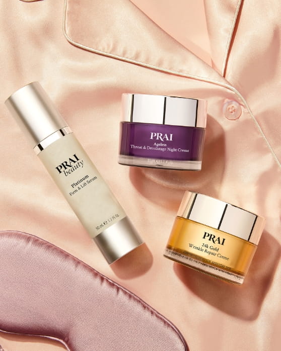 A selection of PRAI Beauty skincare products arranged on pink satin fabric.