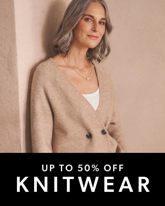 A person wearing a beige double-breasted knit cardigan over a white top, accessorised with a delicate necklace.