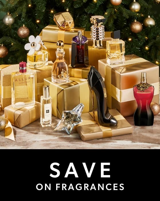 A festive arrangement of perfume bottles displayed among gold-wrapped gift boxes, set in front of a decorated Christmas tree with ornaments.