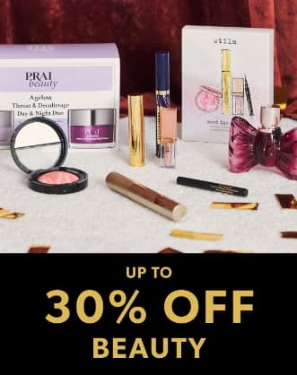 Promotional banner for a beauty sale showing an assortment of cosmetics, including a Prai Beauty Ageless set, Stila makeup kit, perfume, and lip gloss scattered on a white surface with gold confetti.