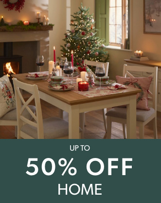 Festive dining room with a wooden table decorated with candles and wine glasses, and a lit Christmas tree and fireplace in the background.