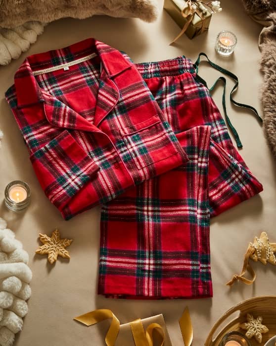 Red plaid pyjama set laid out with candles, ribbons, and festive decorations.